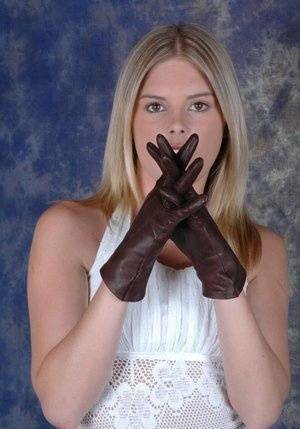 Blonde female pulls on brown leather gloves while wearing a white dress on modelies.com