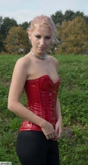 Collared girl Arienh Autumn models a red leather corset while in a field on modelies.com